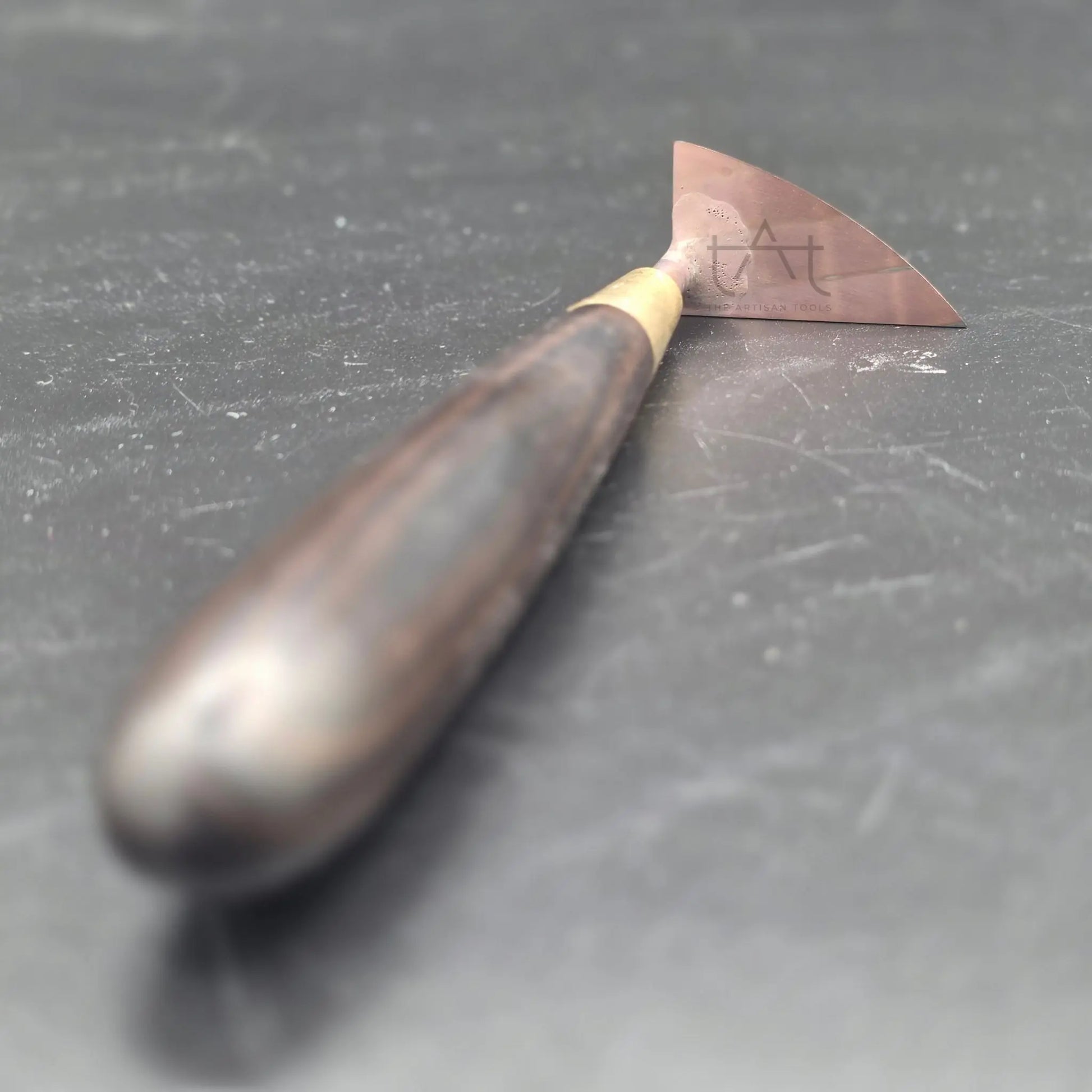 se ve la herramienta de recorte apoyada en la mesa, con el mango de madera en primera toma y la cuchilla de carburo al fondo